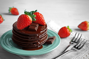 Plate with delicious chocolate pancakes and strawberry on light background