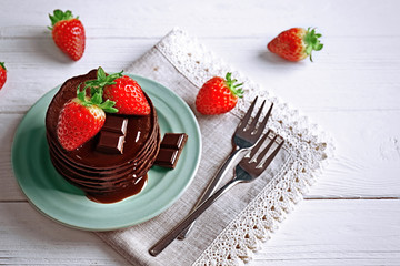 Plate with delicious chocolate pancakes and strawberry on light background