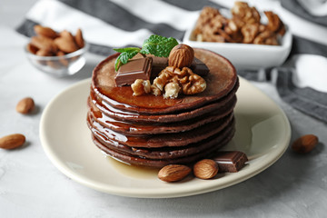 Delicious chocolate pancakes decorated with nuts and sweet syrup on plate