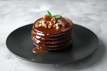Delicious chocolate pancakes decorated with nuts and sweet syrup on black plate