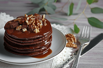 Delicious chocolate pancakes decorated with nuts and sweet syrup on white plate