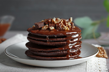 Delicious chocolate pancakes decorated with nuts and sweet syrup on white plate