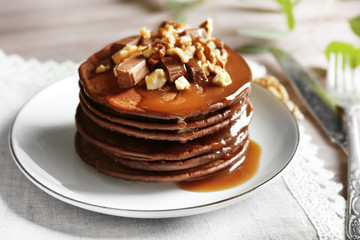 Delicious chocolate pancakes decorated with nuts and sweet syrup on white plate