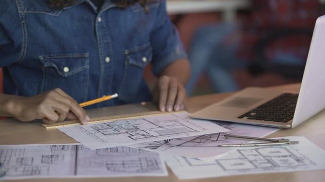 Biracial female designer working on apartment layout plan, drawing line on paper