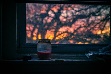 A jar on a windowsill, with a tree and the setting sun outside