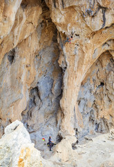 Young man climbing challenging route on cliff, his partner belaying