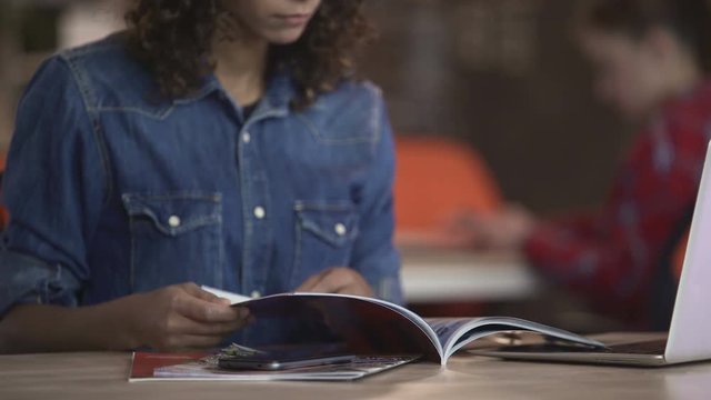 Young biracial woman sitting at beauty salon and viewing pictures in magazine