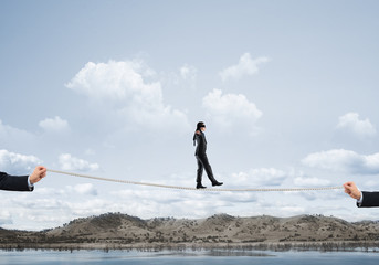 Business concept of risk support and assistance with man balancing on rope