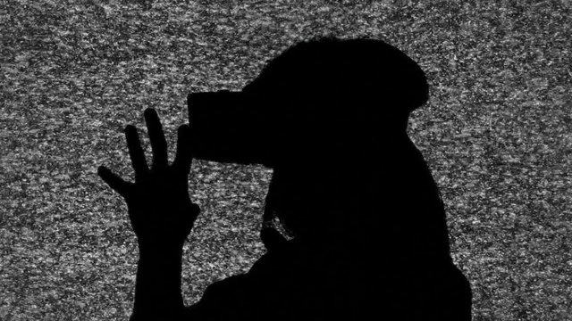 A woman wearing a virtual reality headset. Silhouette shot over the fuzzy noise of an old tv screen.
