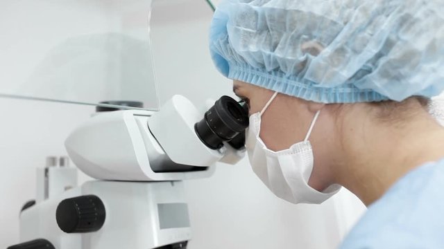 Woman scientist in protective mask look through the microscope in biological laboratory