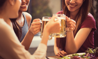 Women are drinking beer and the clink glasses in a restaurant.