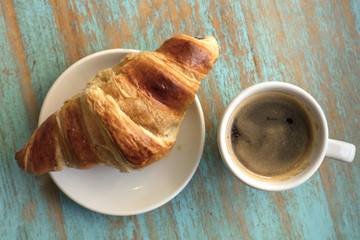 Cup of dark coffee with croissant, on wooden table