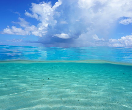 Half and half, Pacific ocean seascape, shallow sandy seabed underwater with cloudy blue sky over the water, French Polynesia
