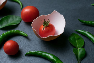 Fresh tomatoes in cracked eggshell on black stone background