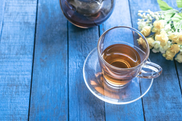 Cup of tea with flower on blue wooden table background.