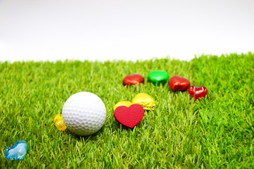 Golf ball and red heart are on green grass.