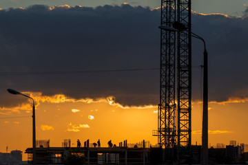 Construction workers silhouettes, cranes and building construction site against sunset sky.