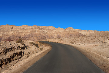 Empty desert road with mountains and blue sky in the background