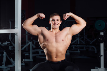 Fototapeta na wymiar professional fitness bodybuilder sitting on the bench and demonstrates muscles of your body after a workout, at gym.