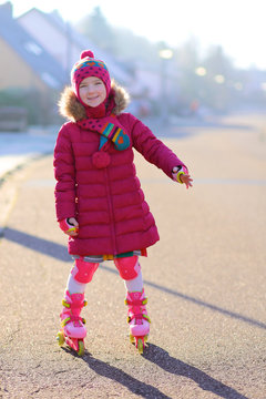 Little girl on roller skates. Child having fun skating outdoors on the sunny day. Kid playing safe on the street.