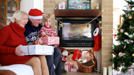 Happy family exchanging christmas gifts in decorated living room with xmas tree and fireplace....