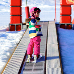Happy child enjoying winter vacation in Alpine resort in Austria. Active sportive toddler girl learning to ski. Kid having fun in ski school going up to the slope on the magic carpet lift.