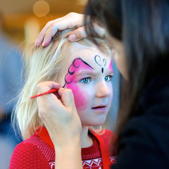 Cute little girl getting her face painted like a butterfly by face painting artist. Kids animation...