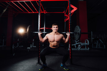 Fototapeta na wymiar portrait of a handsome athlete at gym. man does the exercise with barbell, standing and squatting. big confident