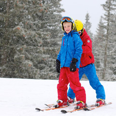 Two happy school boys, twin brothers in colorful snowsuits, having fun skiing in alpine mountains during snowy winter vacation