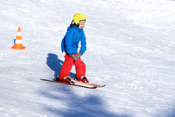 Fototapeta na wymiar Happy school boy in colourful snowsuit learning to ski in alpine resort on sunny day during winter vacation