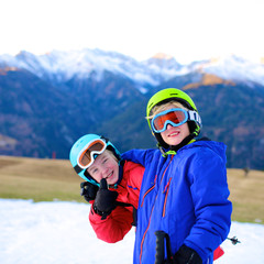 Happy children enjoying winter holidays in Alpine resort in Austria. Two brothers playing in the snow. Active sportive boys learning to ski. Beautiful Alps mountains in the background.