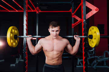 Fototapeta na wymiar portrait of a handsome athlete at gym. man does the exercise with barbell, standing and squatting. big confident