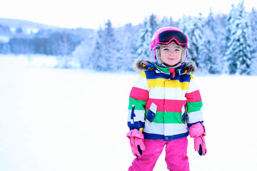 Fototapeta na wymiar Happy child enjoying vacation in Alpine resort in Austria. Little girl skiing in mountains. Active sportive toddler wearing helmet and glasses learning to ski. Winter sport for family.