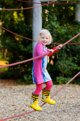Happy kid enjoying active day outdoors. Adorable little child, blond cute toddler girl, having fun in the park climbing on rope playground on a sunny day