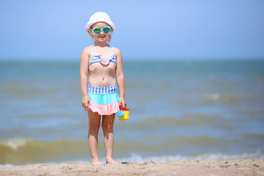 Adorable toddler girl in pretty  swimsuite playing with toys on wide sandy beach