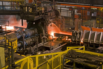 Hot steel being rolled to shape in mill in steel manufacturing plant.