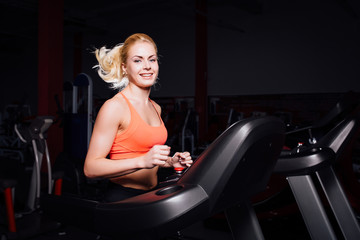 Fototapeta na wymiar Young beautiful cute girl in fitness model in the gym running on the treadmill with bottle