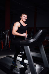 Fototapeta na wymiar Young strong big man fitness model in the gym running on the treadmill with water bottle.