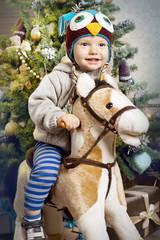 A little boy plays with a horse-rocking around the Christmas tree