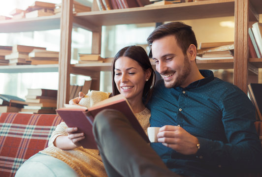 Young couple drinking coffee in cafeteria, surrounded with books