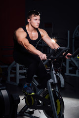 Fototapeta na wymiar Portrait of a handsome man workout on fitness the exercise bike dark at gym.
