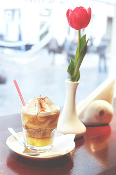 Cup of tasty creamy frappuccino or coffee coctail dessert and vase with a flower in cafe