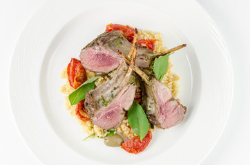 Rack of lamb with bulgur, dried tomatoes and lemon Moroccan on a plate on a white background, top view closeup