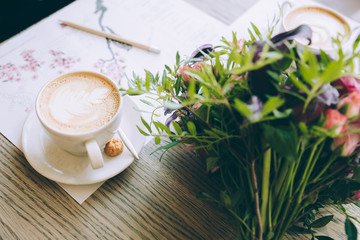 Still life with cup of coffee and flowers on wooden table.