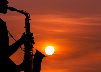 Obraz premium silhouette young woman playing the saxophone in sunset