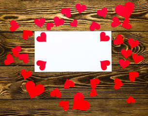 Holiday/romantic/wedding/valentine Day background with small paper red hearts and blank message card on wooden table.