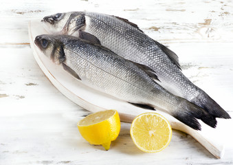 Two raw seabass with lemon on a wooden background.