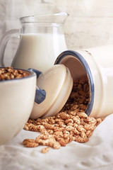 Puffed barley cereal spilling from jar with pitcher of milk in background