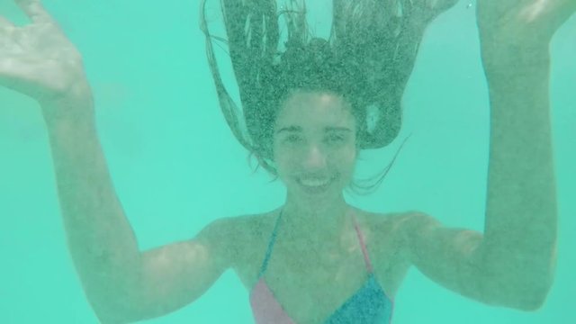 Caucasian beautiful female with long dark hair diving in pool smiling laughing hand kissing. Close up underwater footage in slowmotion