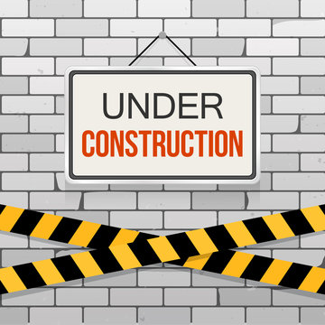 Simple white sign with text 'Under Construction' hanging on a gray brick wall with warning tapes. Grunge brickwork background. Building, engineering concept. Creative template for web design